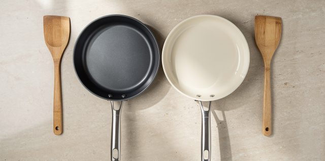 Deux poêles antiadhésives vues de dessus sur un plan de travail de cuisine, l’une sombre avec un revêtement aspect titane et l’autre claire avec un revêtement aspect céramique, accompagnées de spatules en bois.